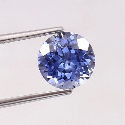 Paste Blue Color Sapphire gemstone held by tweezers on a light gray background