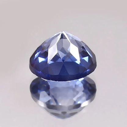 Faceted Paste Blue Color Sapphire gemstone on a reflective surface with a light gray background