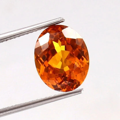 Orange Sapphire gemstone held between tweezers on a white background