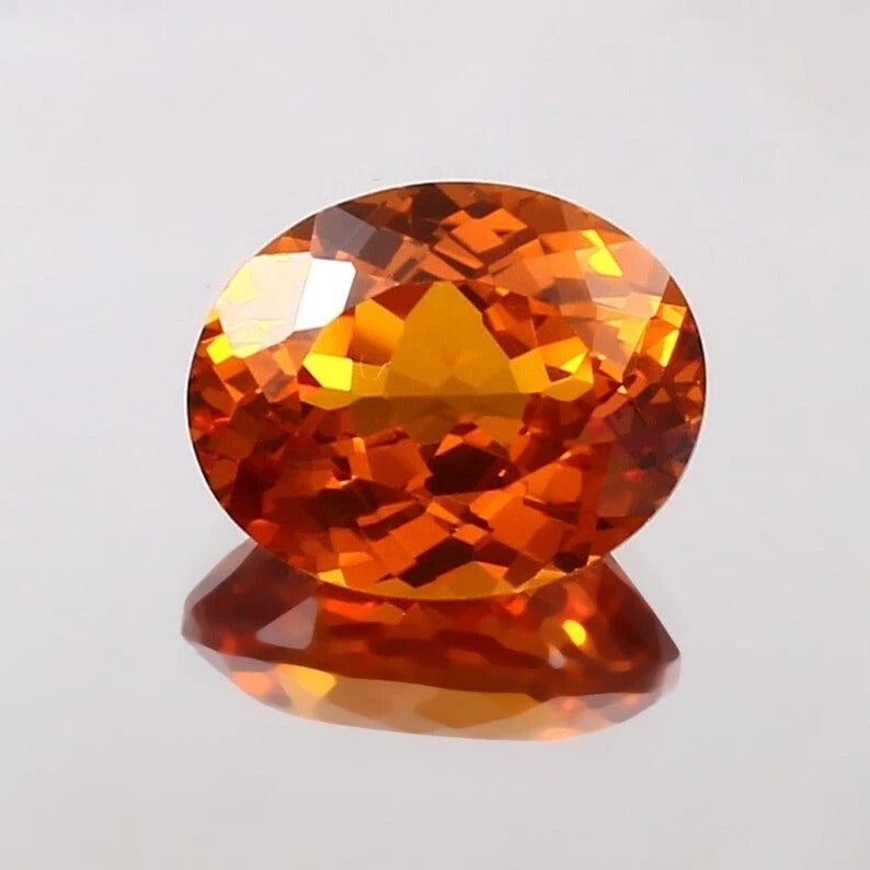 Faceted Sapphire orange-red gemstone on a light gray background