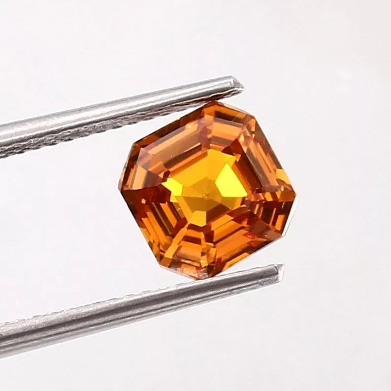 Ceylon Fanta Orange Sapphire Untreated gemstone held by tweezers on a white background
