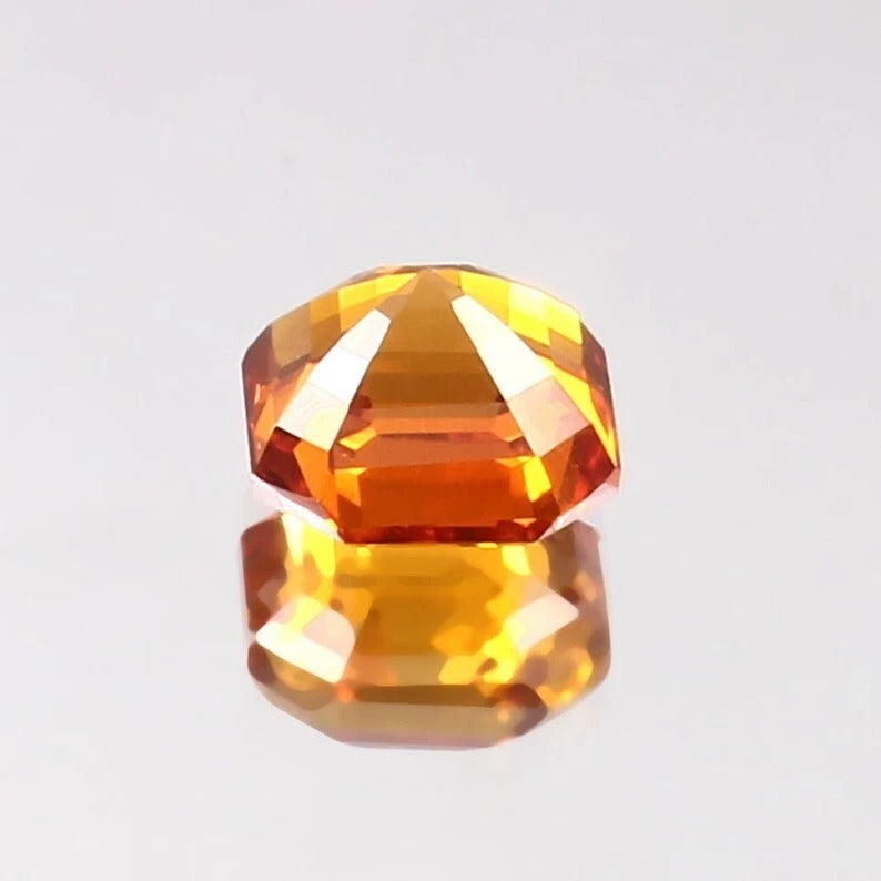 Faceted Ceylon Fanta Orange Sapphire Untreated gemstone on a reflective surface with a light gray background