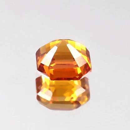 Faceted Ceylon Fanta Orange Sapphire Untreated gemstone on a reflective surface with a light gray background