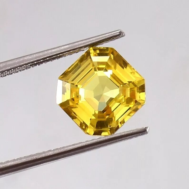 Yellow Sapphire Asscher gemstone held by tweezers on a light gray background
