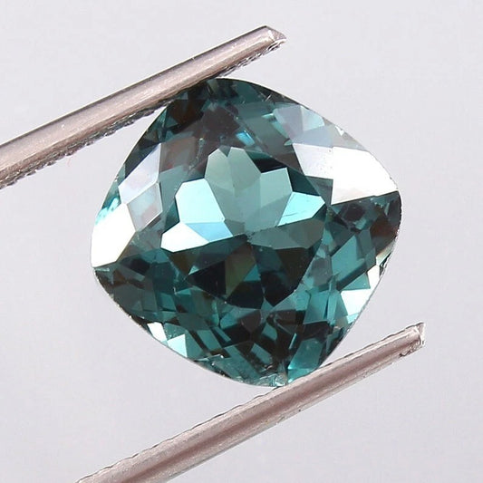 Indicolite Tourmaline gemstone held between tweezers on a light gray background