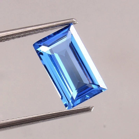 Blue Brazilian Aquamarine Baguette Cut gemstone held by tweezers on a gray background