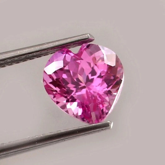 Heart-shaped pink sapphire  gemstone held by tweezers on a gray background