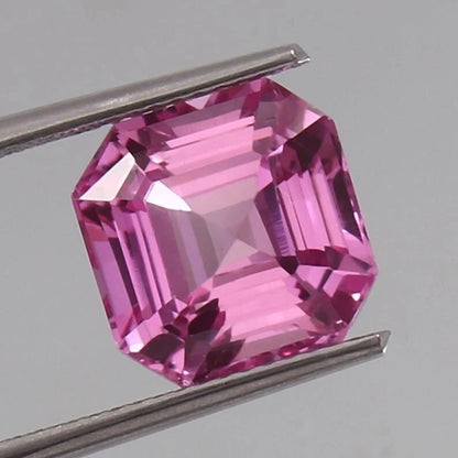 Pink Sapphire Unheated gemstone held between tweezers against a gray background