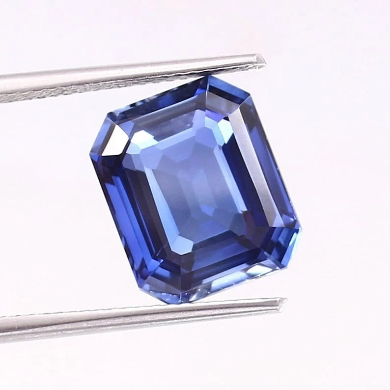 Blue Sapphire gemstone held by tweezers on a white background