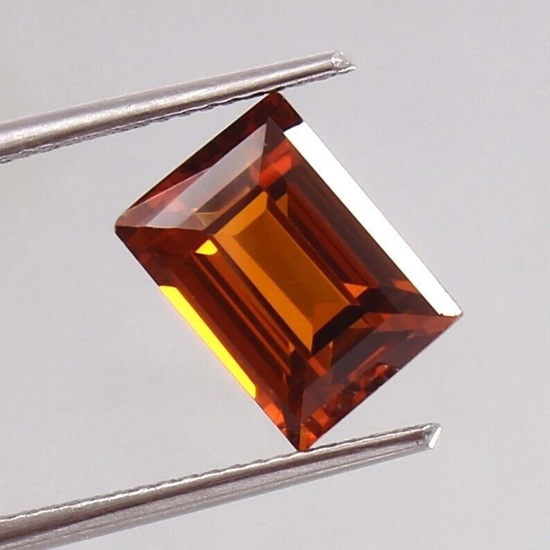 Baguette orange sapphiregemstone held between tweezers on a gray background
