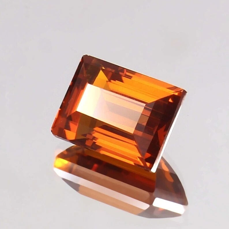 Baguette orange sapphire gemstone on a reflective surface with a light gray background