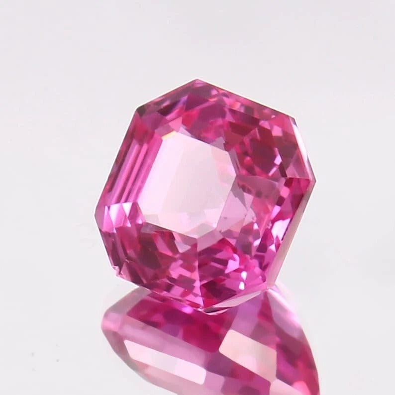 Faceted Pink Sapphire asscher gemstone on a reflective surface with a light gray background