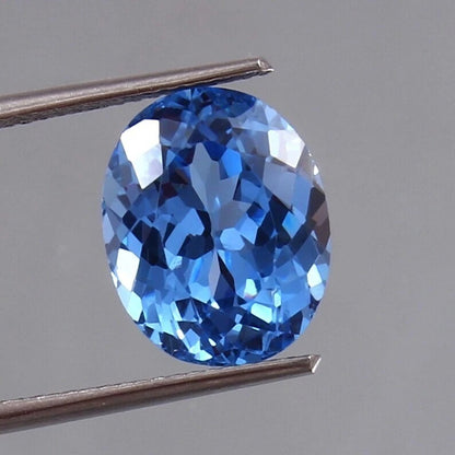 Blue Tourmaline Unheated gemstone held between tweezers against a gray background