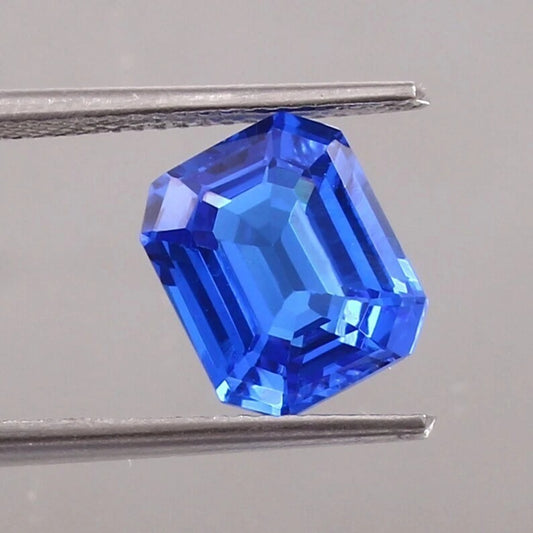 Faceted Cornflower Blue Sapphire gemstone held between tweezers on a neutral background