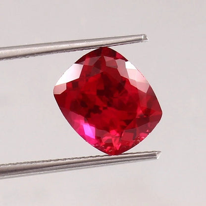 Faceted Pigeon Blood Ruby gemstone held by tweezers on a light gray background
