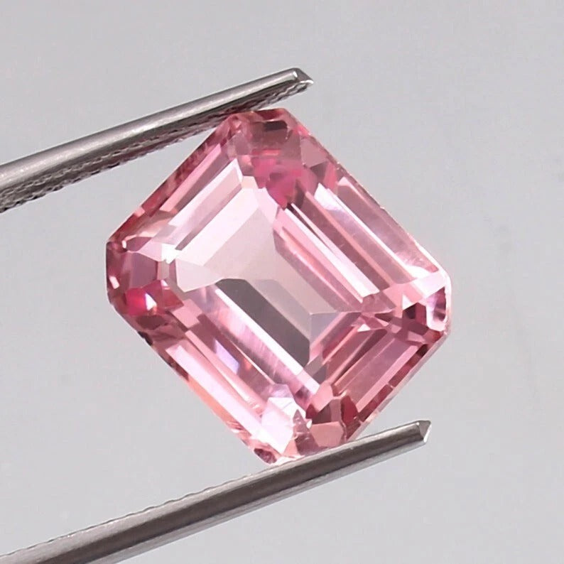 Padparadscha Sapphire gemstone held between tweezers against a gray background