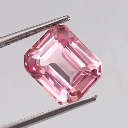 Padparadscha Sapphire gemstone held between tweezers against a gray background