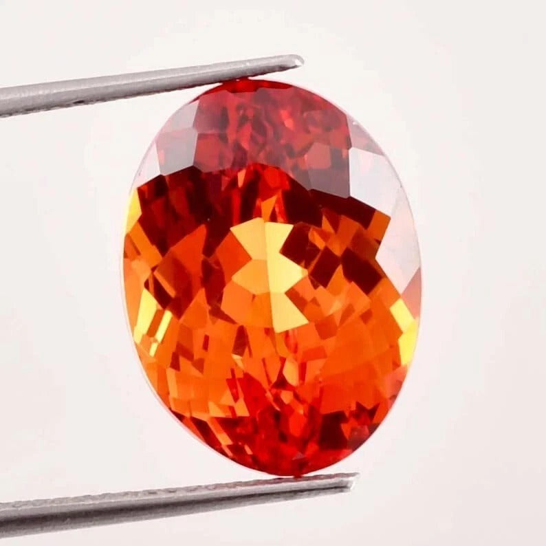 Fanta Orange Sapphire gemstone held by tweezers on a white background
