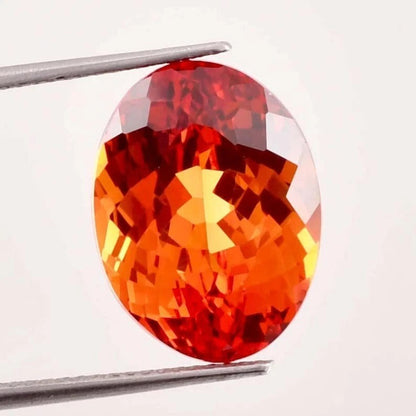 Fanta Orange Sapphire gemstone held by tweezers on a white background