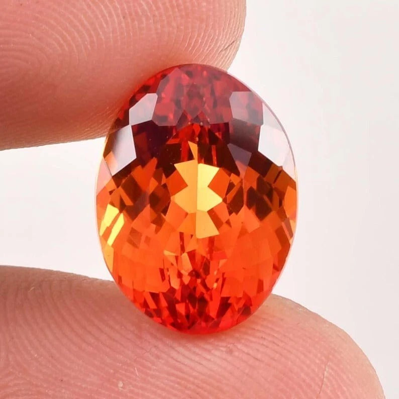 Faceted Fanta Orange Sapphire gemstone held between two fingers against a white background