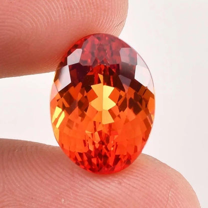 Faceted Fanta Orange Sapphire gemstone held between two fingers against a white background