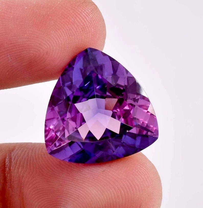 Bi-Color Purple Sapphire gemstone held between fingers against a white background