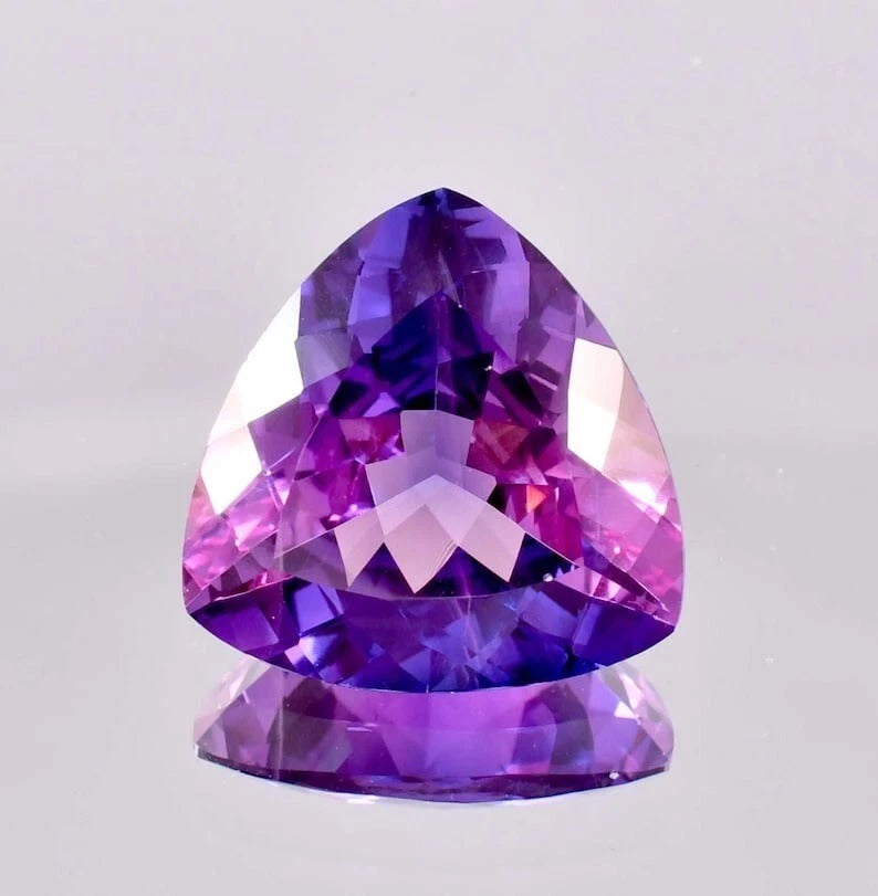 Trillion-shaped Bi-Color Purple Sapphire gemstone on a light gray background