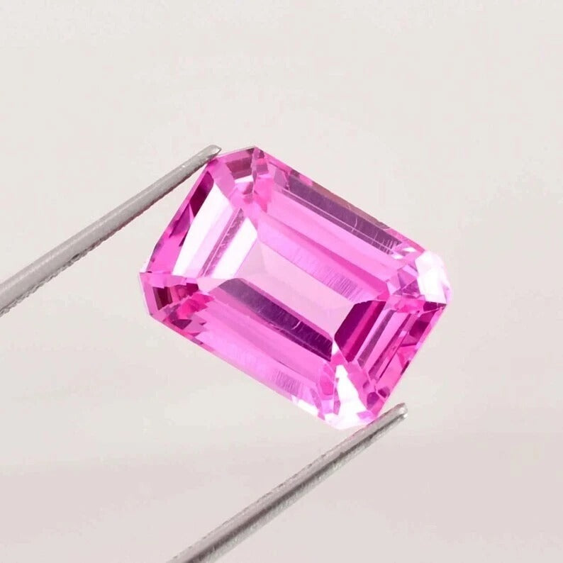 Pink Ceylon Sapphire gemstone held by tweezers on a light gray background