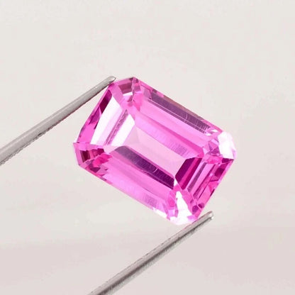 Pink Ceylon Sapphire gemstone held by tweezers on a light gray background