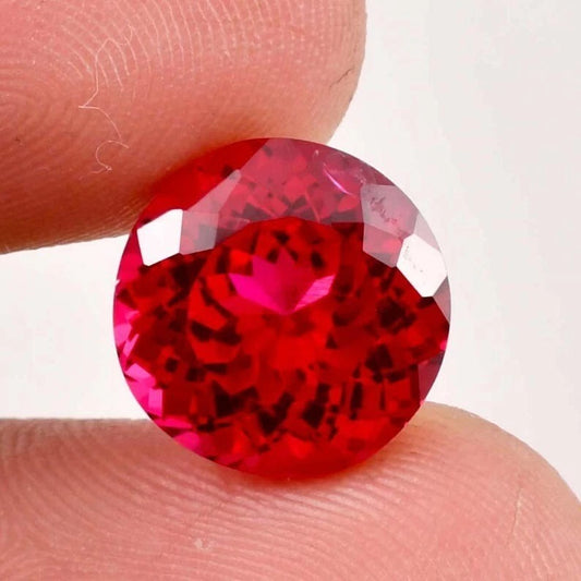 Red ruby gemstone held between two fingers against a white background