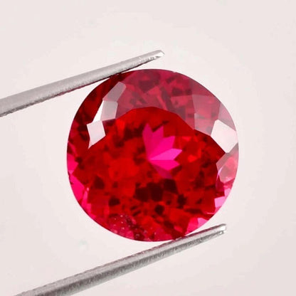 ruby Round red gemstone held by tweezers on a light gray background