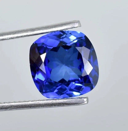Blue Sapphire cushion gemstone held by tweezers on a light gray background