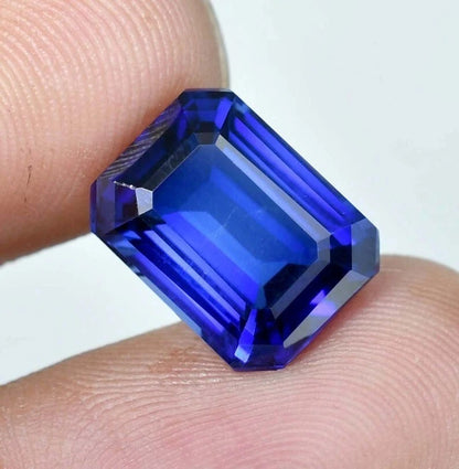 Royal Blue Sapphire gemstone held between two fingers against a white background