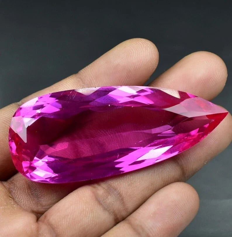 Hand holding a large Royal Pink Ceylon Sapphire gemstone against a dark background