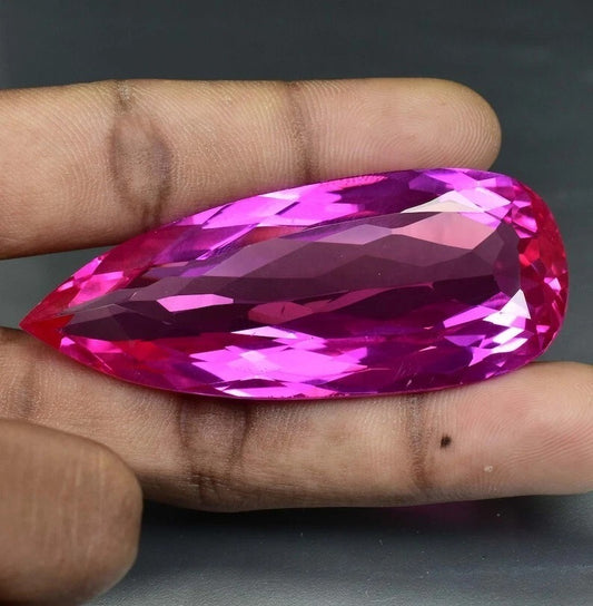 Faceted Royal Pink Ceylon Sapphire gemstone held between fingers against a dark background