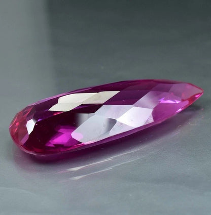 Faceted Royal Pink Ceylon Sapphire gemstone on a gray background
