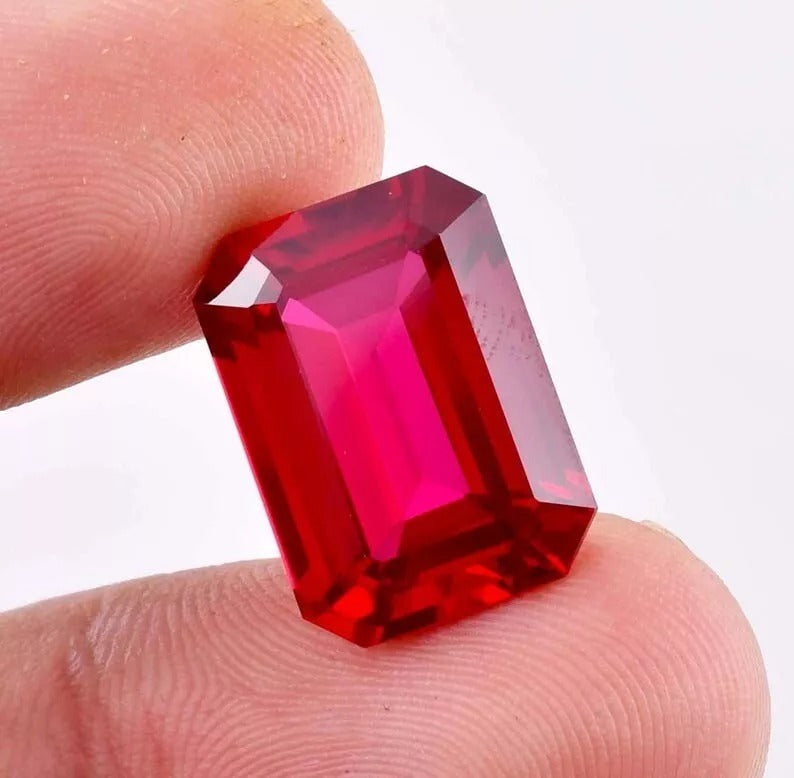 Red Pigeon Blood Ruby gemstone held between fingers against a white background