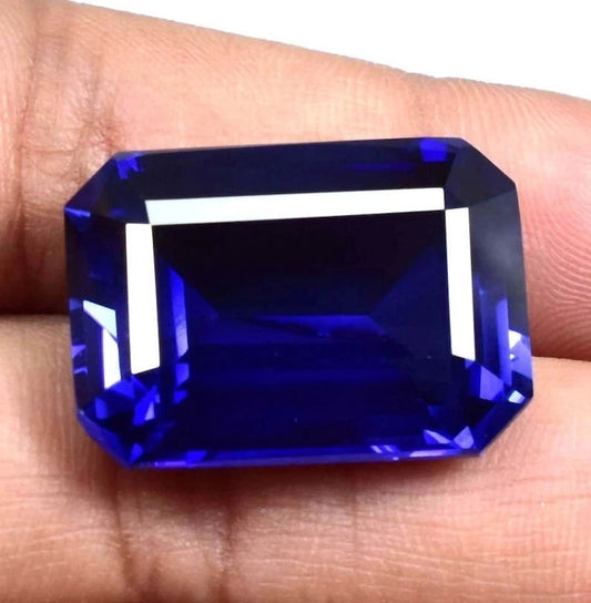 Faceted blue Sapphire gemstone held between fingers against a neutral background