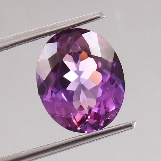 Taaffeite gemstone held between tweezers on a light gray background