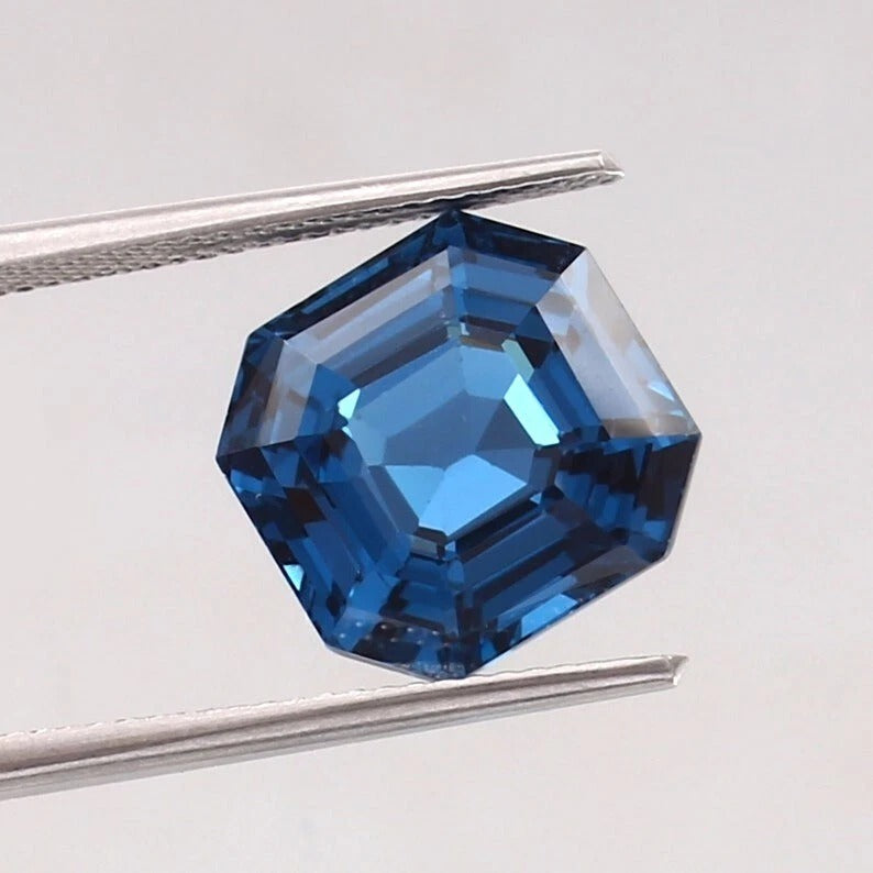 Blue Tourmaline gemstone held between tweezers on a light gray background