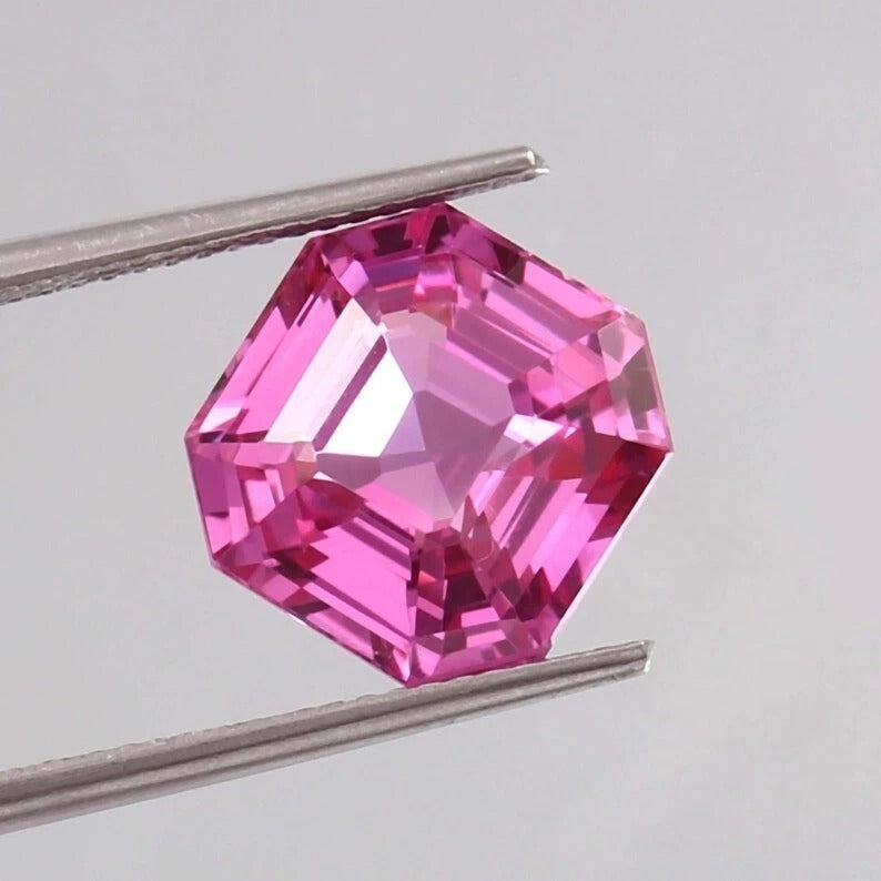 Flawless Ceylon Pink Sapphire gemstone held between tweezers against a light gray background