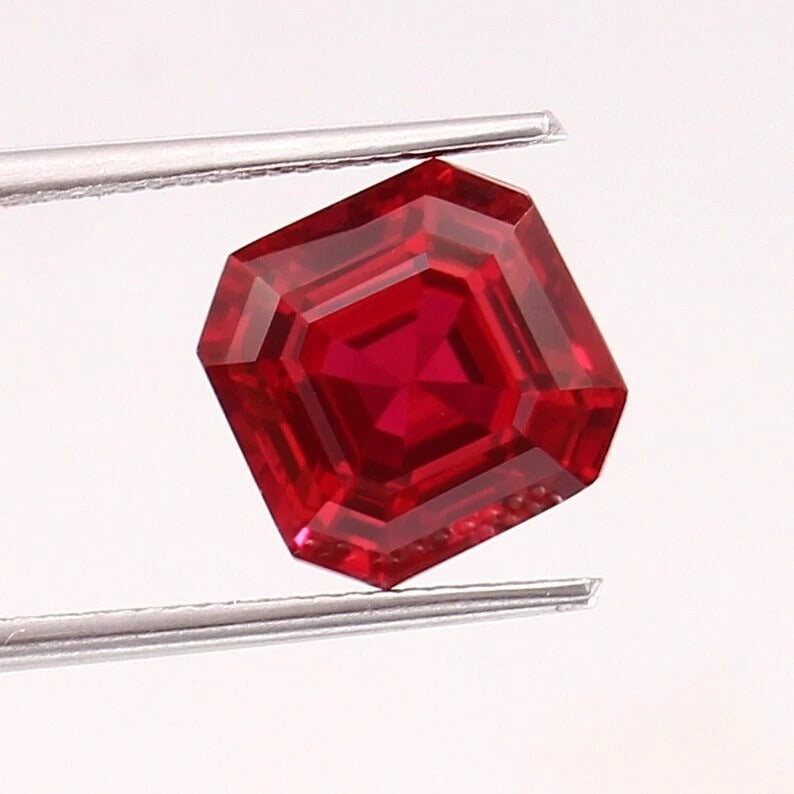 Red ruby Mogok gemstone held by tweezers on a white background