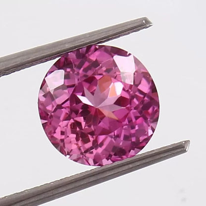 Round Pink Sapphire gemstone held between tweezers on a light gray background