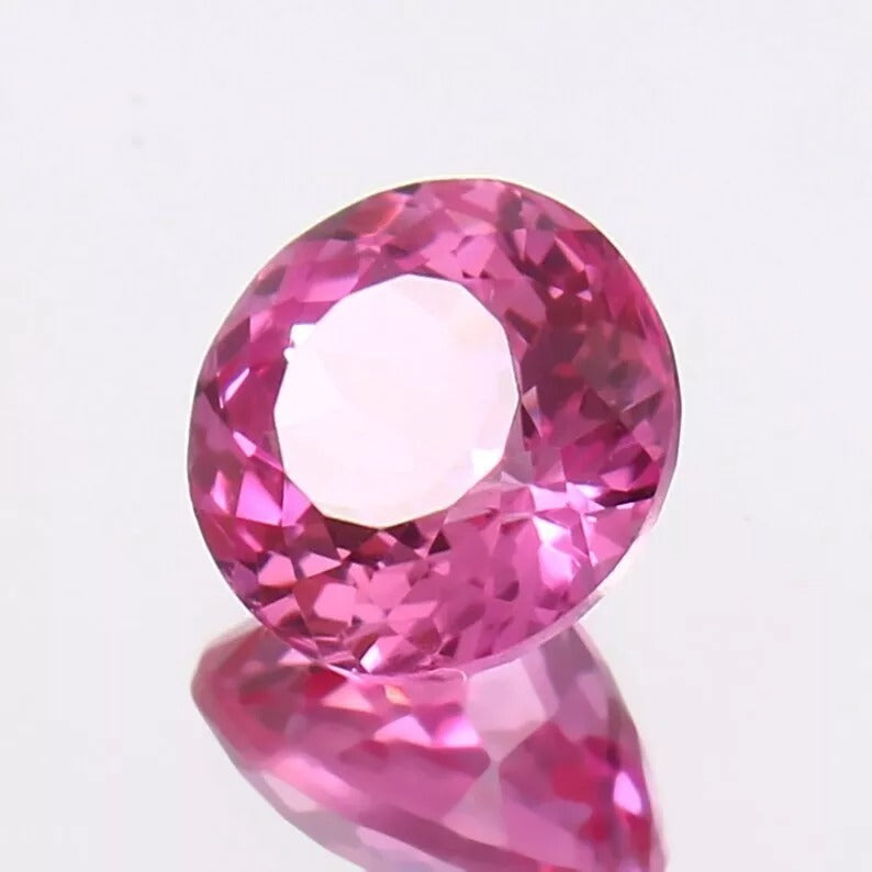 Pink Sapphire gemstone on a reflective surface with a light gray background