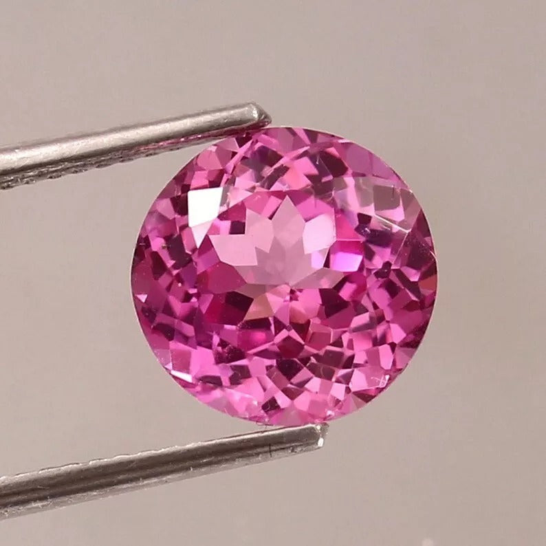 Ceylon Pink Sapphire gemstone held by tweezers against a neutral background