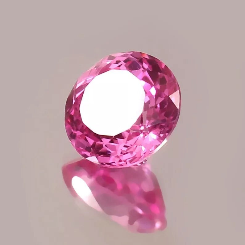Ceylon Pink Sapphire gemstone on a reflective surface with a neutral background