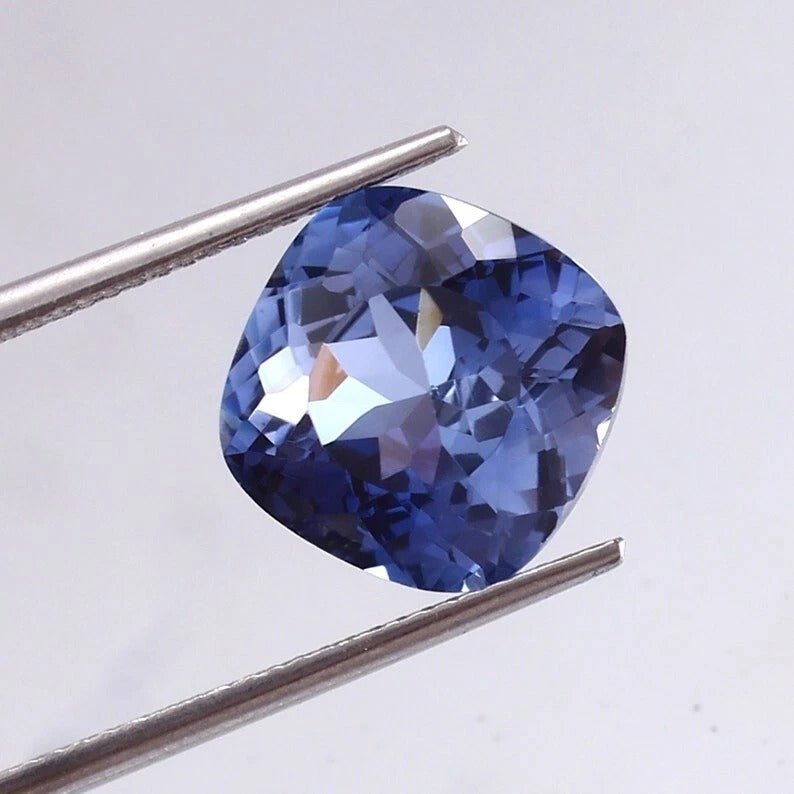  Blue Sapphire gemstone held between tweezers on a light gray background