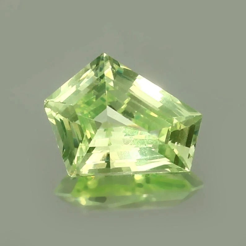 Green Chrysoberyl  gemstone with a faceted cut on a gray background