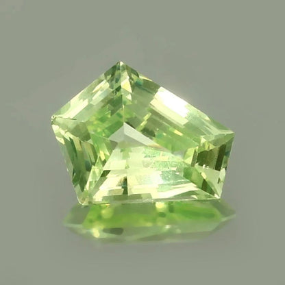 Green Chrysoberyl  gemstone with a faceted cut on a gray background