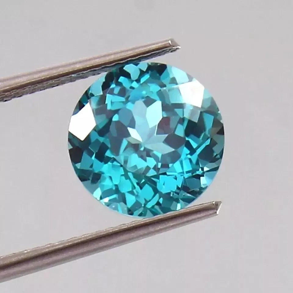 Parti Sapphire gemstone held between tweezers on a light gray background